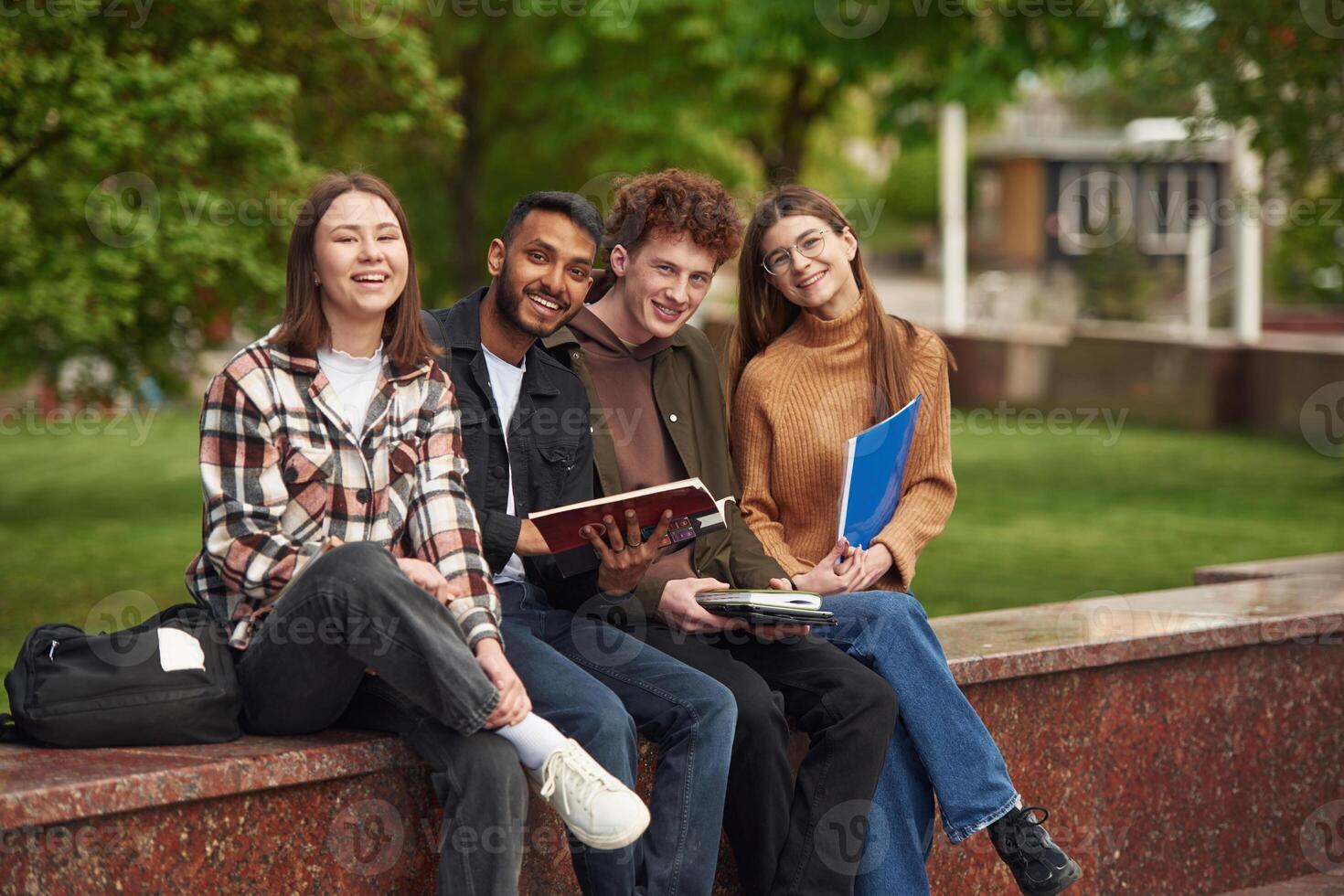 Sitting ,and smiling. Four young, students in casual clothes are together outdoors photo