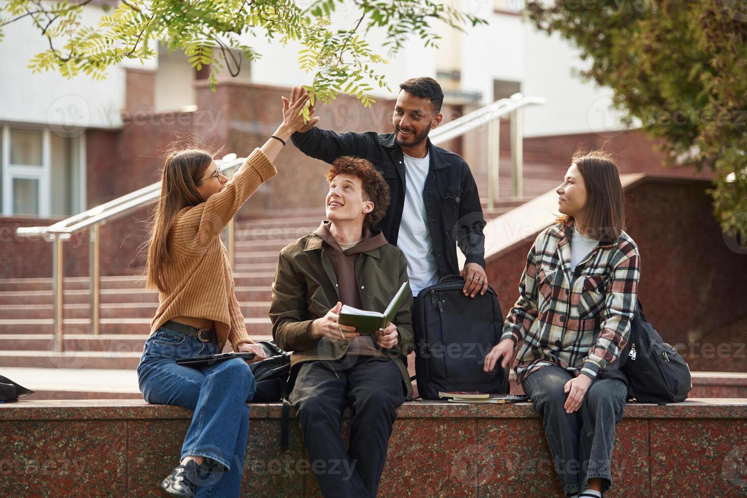 Doing high five. Four, young, students in casual clothes are together outdoors photo