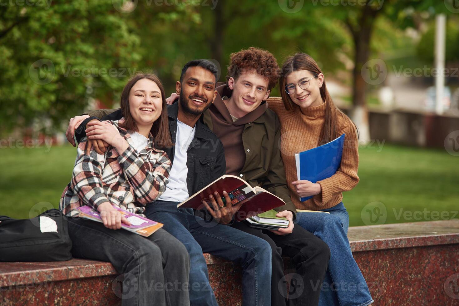 Sitting and smiling. Four young students, in casual clothes are together outdoors photo