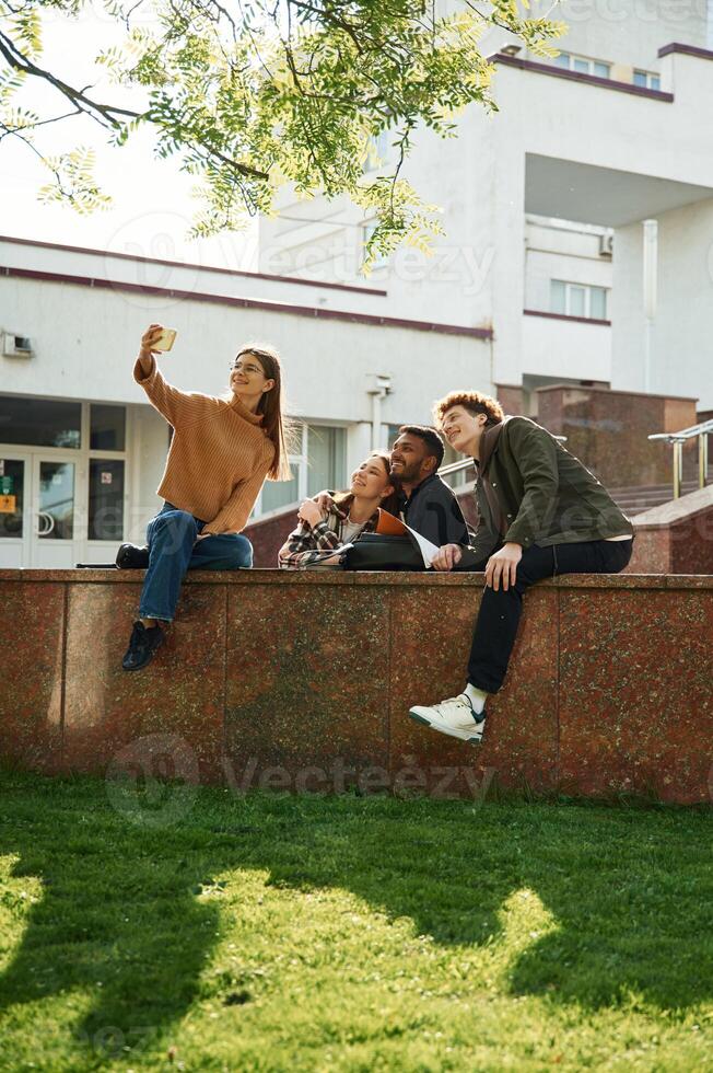 Tree with, green leaves. Four young students in casual clothes are together outdoors photo