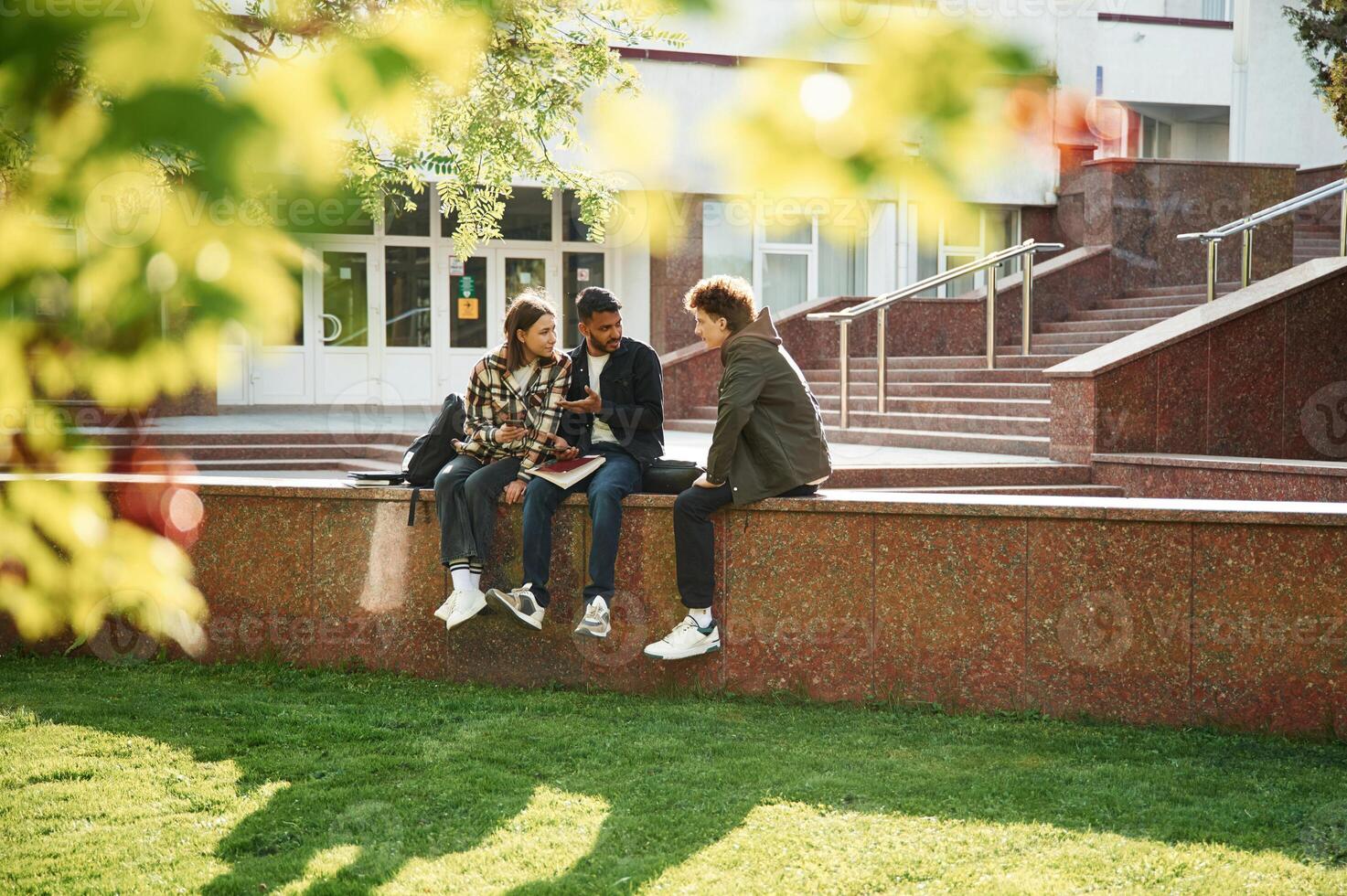 University building is behind. .Young ,students in casual clothes are together outdoors photo
