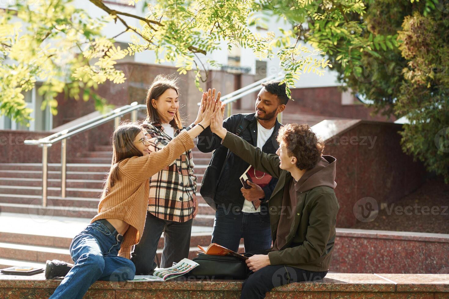 Doing, high, five. Four young students in casual clothes are together outdoors photo