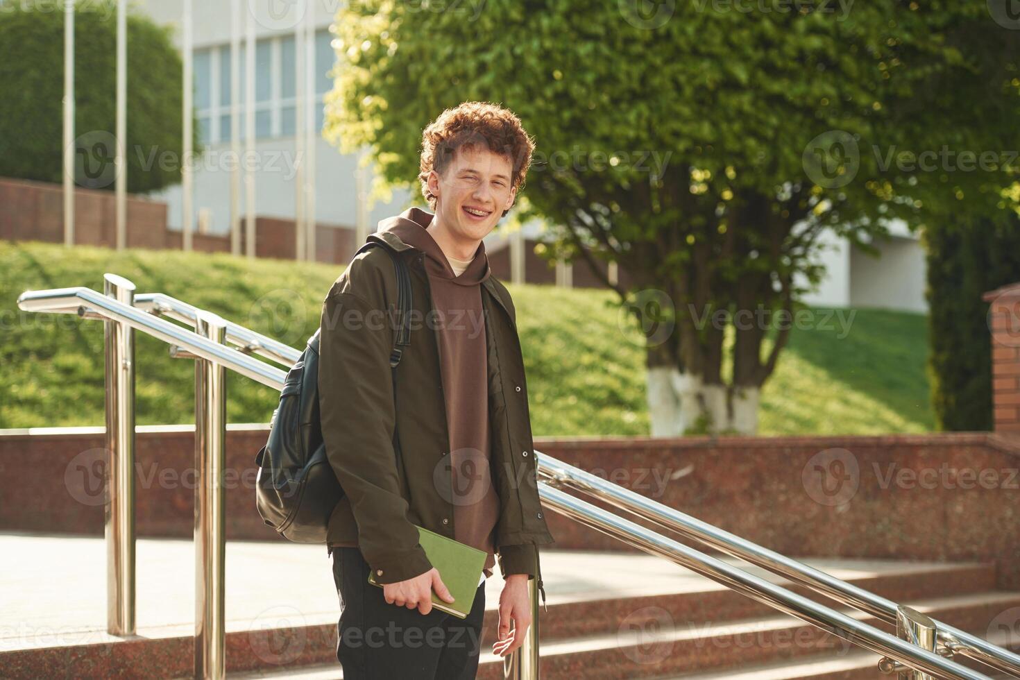 With backpack.. Young student with curly hair is outdoors near university photo