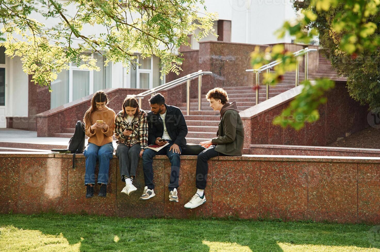 Tree with ,green leaves. Four young students in casual clothes are together outdoors photo