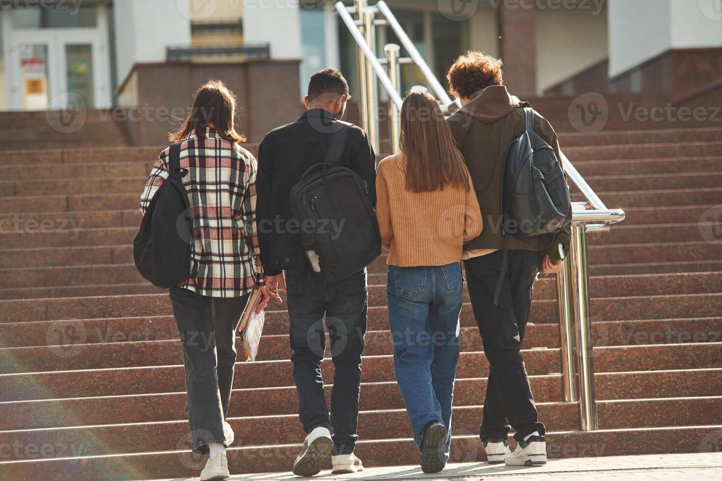 View, from ,back, walking together. Four young students in casual clothes are outdoors photo