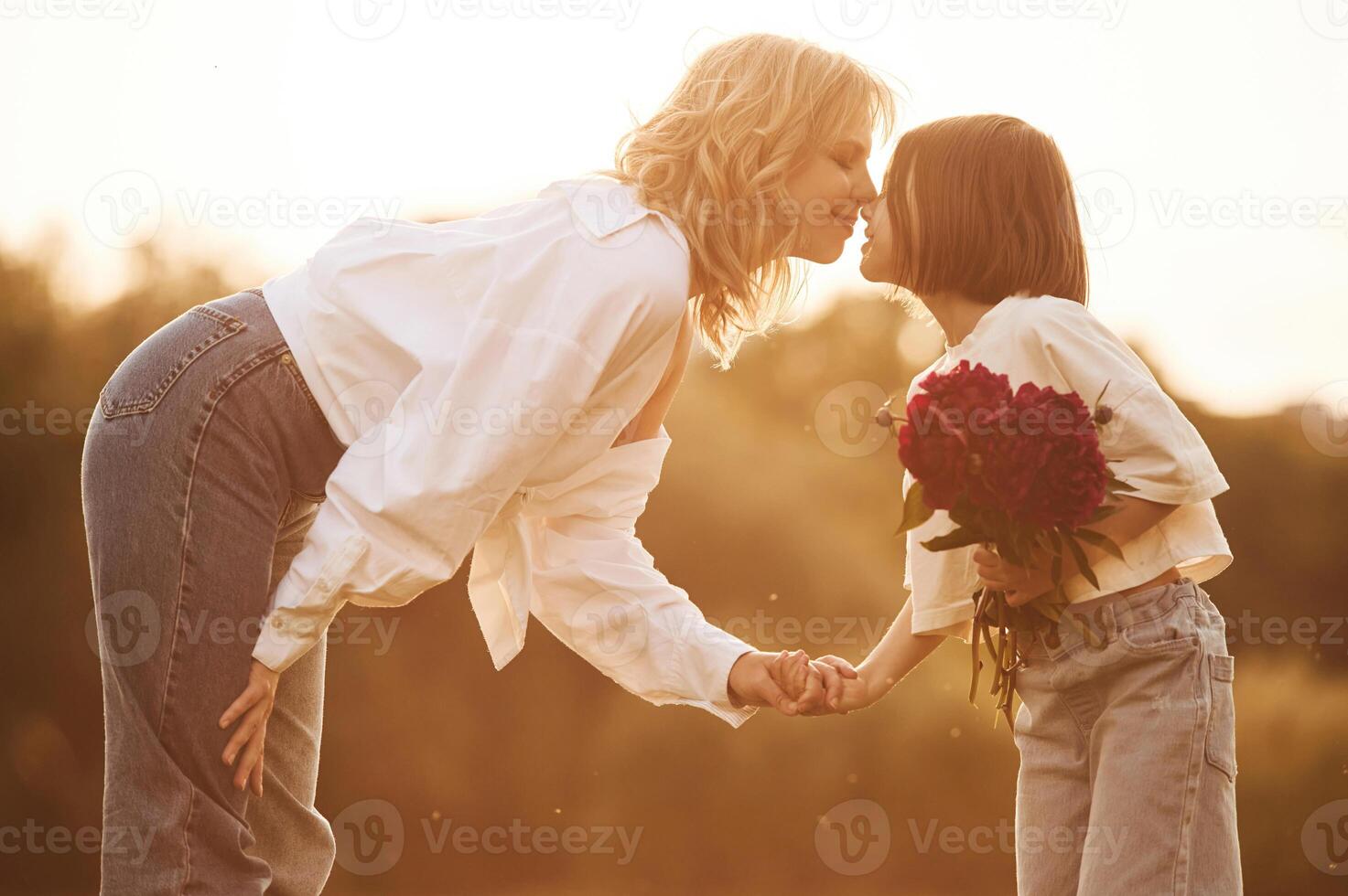 Kid, is holding red flowers. Woman with ,her little daughter are on the summer field together photo