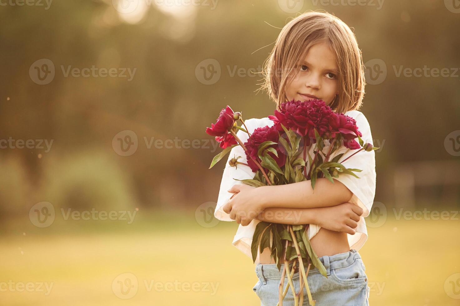 Holding beautiful red flowers.. Little girl is on the summer field at daytime photo