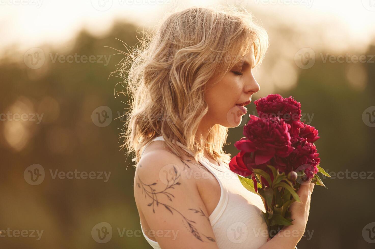 Side, view. Beautiful, young woman is standing outdoors and holding red flowers photo