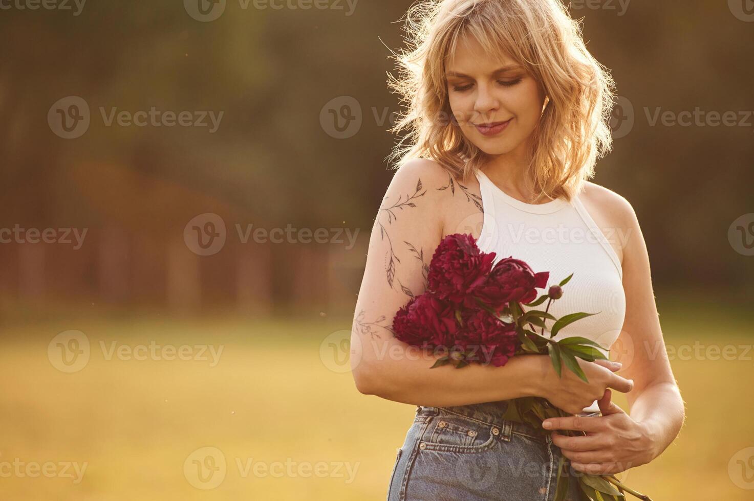 Portrait of ,beautiful young woman that is standing outdoors and holding red flowers photo