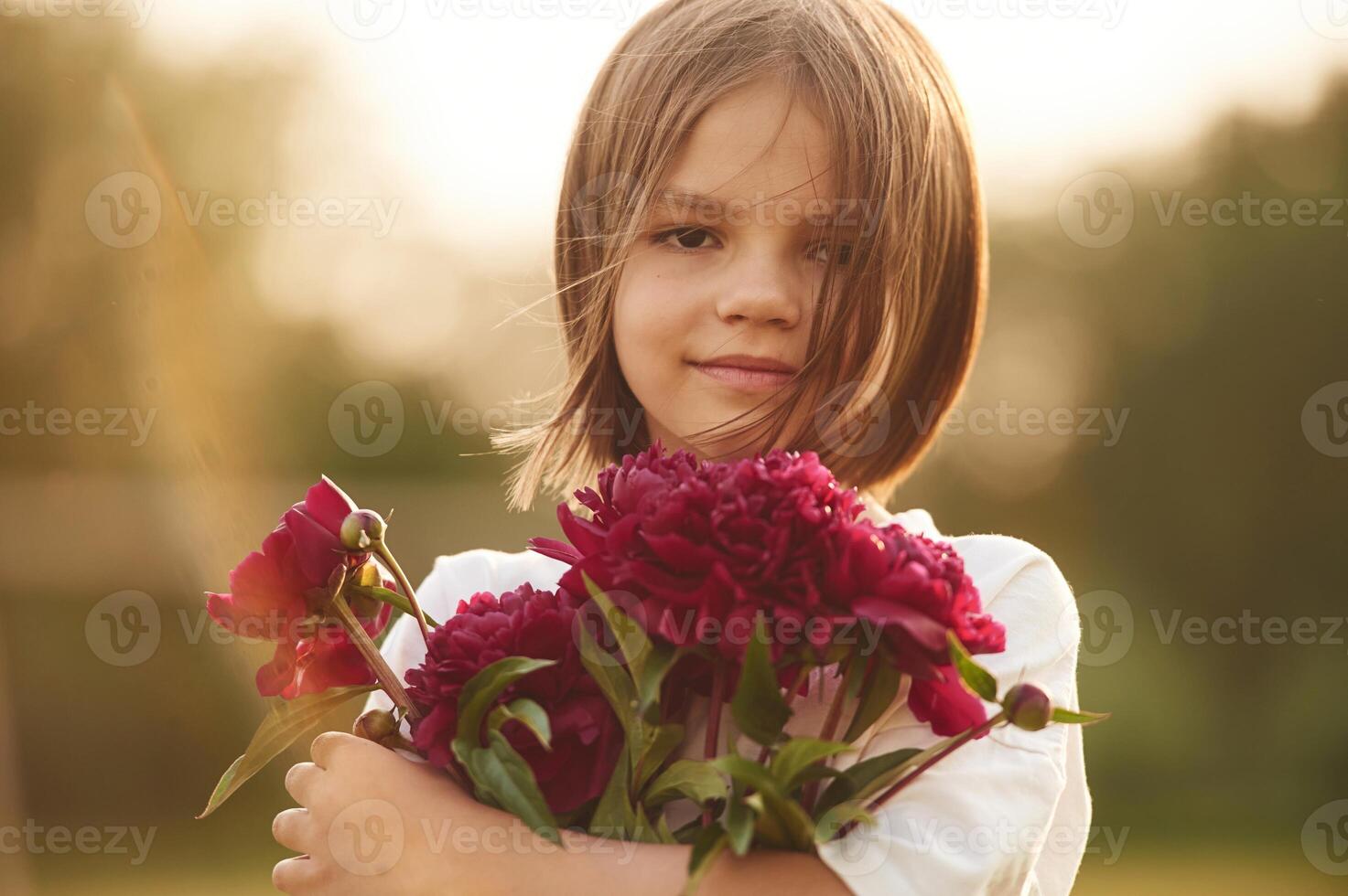 Portrait, standing, and holding red flowers. Little girl is on the summer field at daytime photo