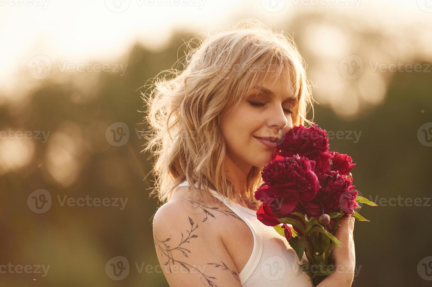 Beautiful, young woman is standing outdoors and holding red flowers photo