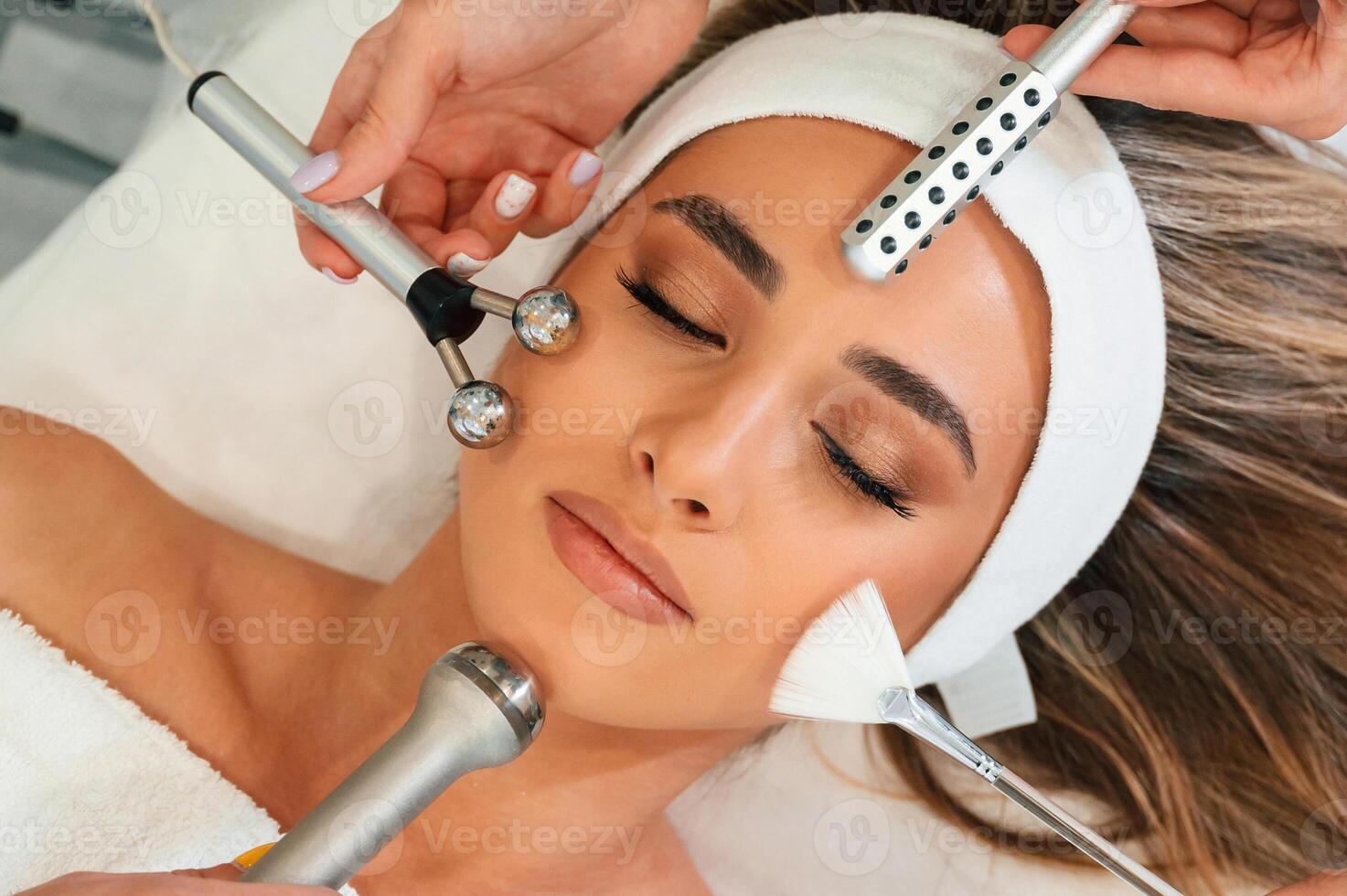 Many, of different ,cosmetitian tools. Woman face getting facial care by beautician hands at spa salon photo