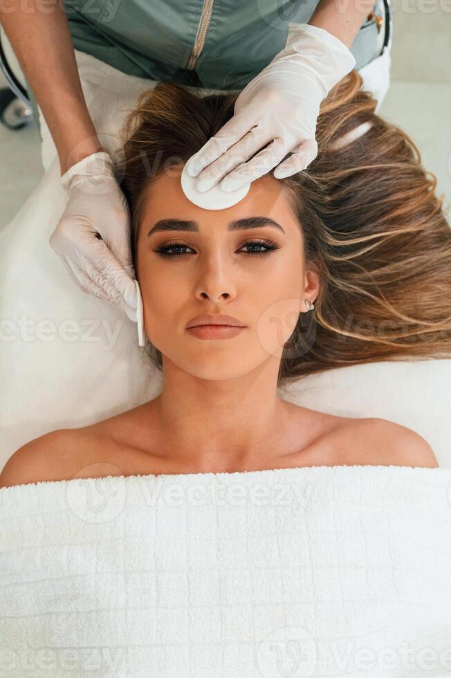 Cotton, pad or sponge are ,used to ,clean the skin. Woman face getting facial care by beautician hands at spa salon photo