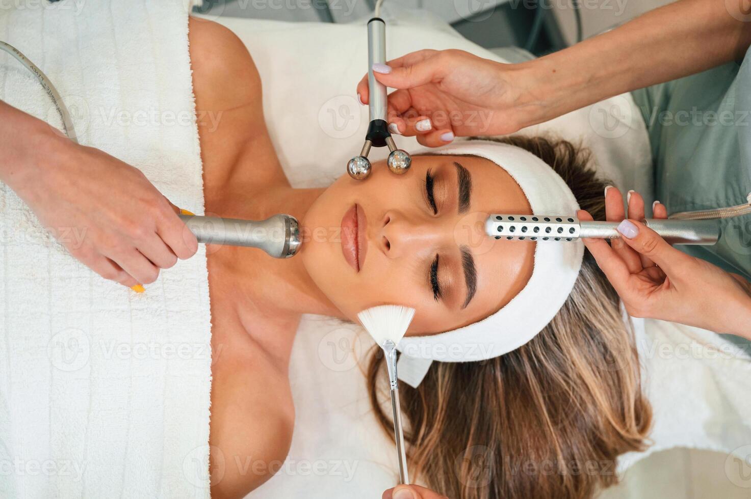 Many, of different cosmetitian tools. Woman face getting facial care by beautician hands at spa salon photo