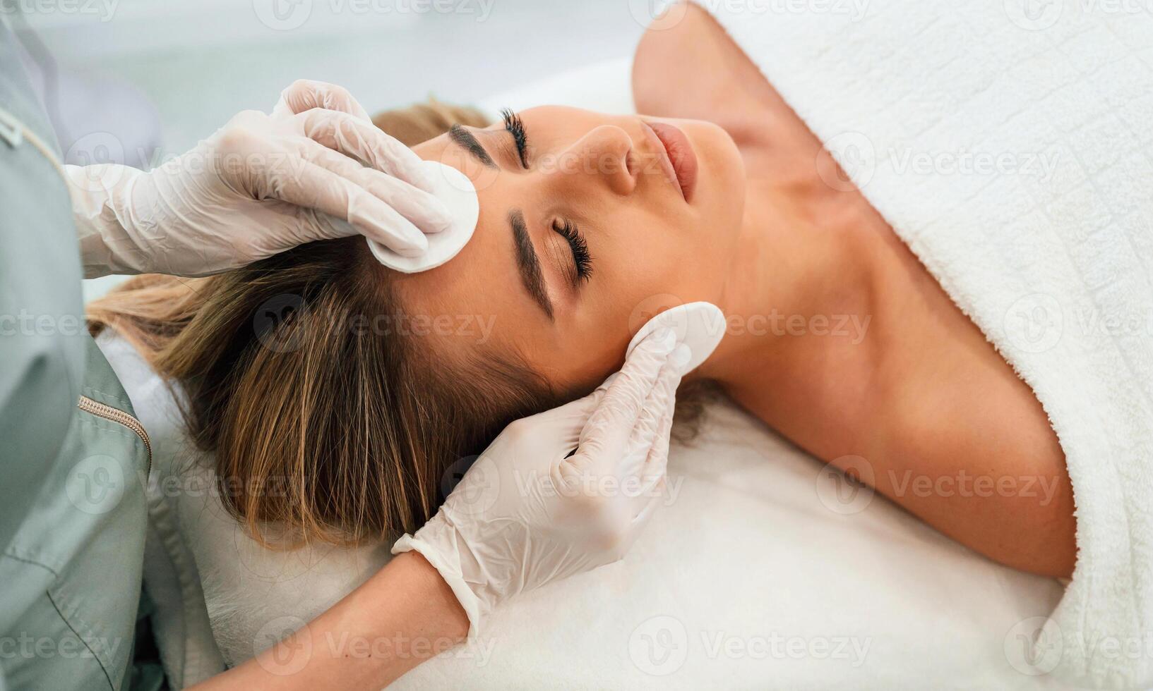 Cotton ,pad ,or sponge are used to clean the skin. Woman face getting facial care by beautician hands at spa salon photo