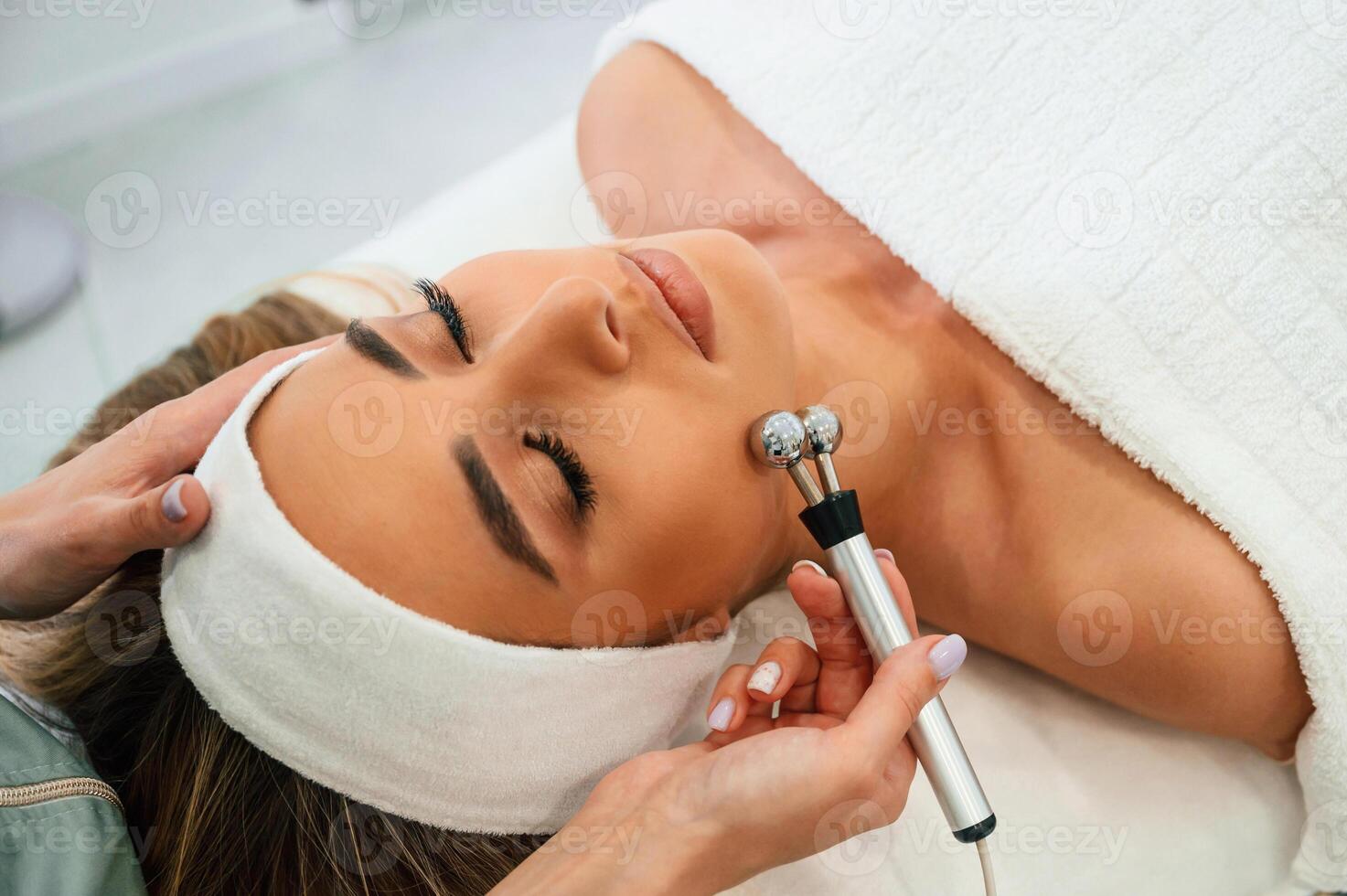 Massage roller ,is used. Woman, face getting facial care by beautician hands at spa salon photo