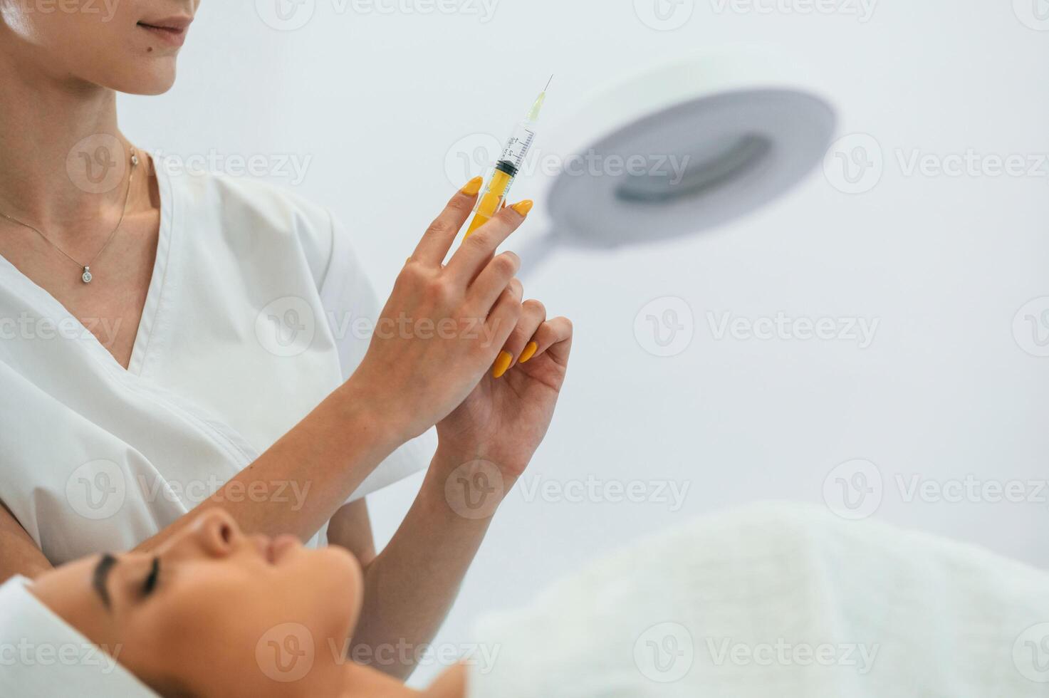 Holding a syringe. Woman face getting facial care by beautician at spa salon photo