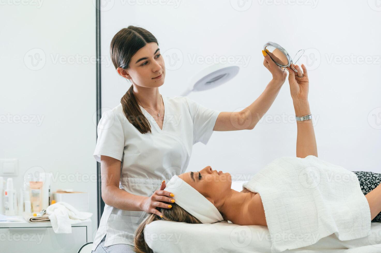 Taking a look in the mirror. Woman face getting facial care by beautician hands at spa salon photo