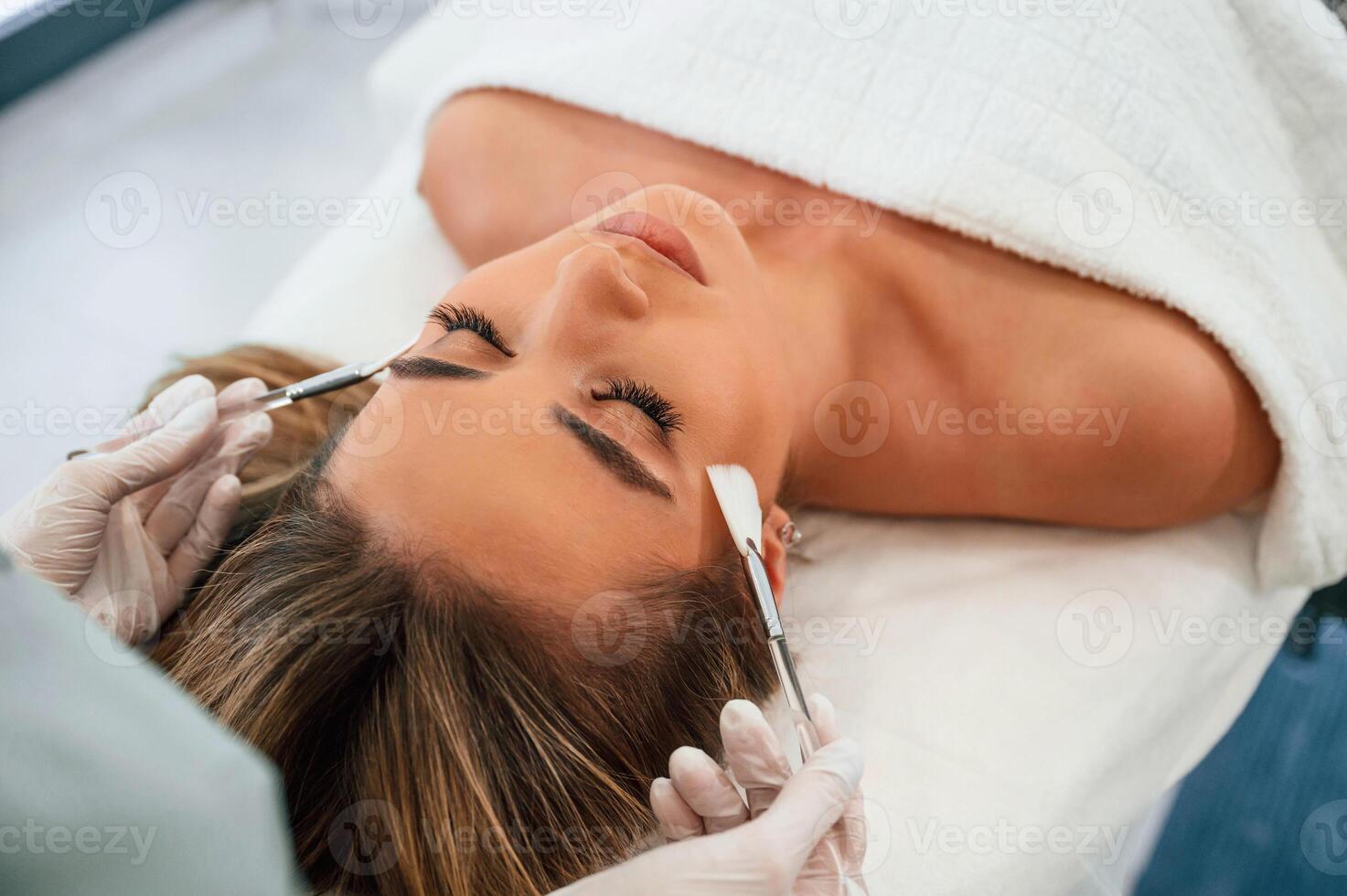 Brushes, are used to clean skin. Woman face getting facial care by beautician hands at spa salon photo