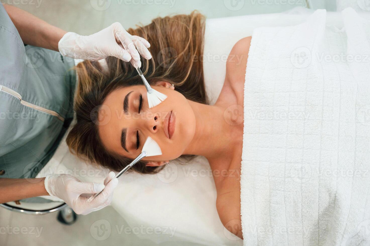 Top view,, using brushes. Woman face getting facial care by beautician hands at spa salon photo