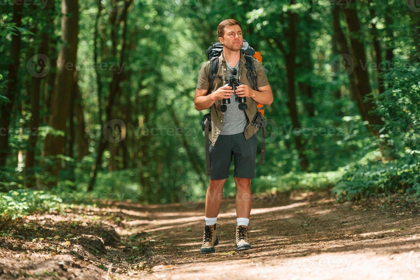 Standing and holding binoculars. .Tourist in summer forest. Conception of exploration and leisure photo