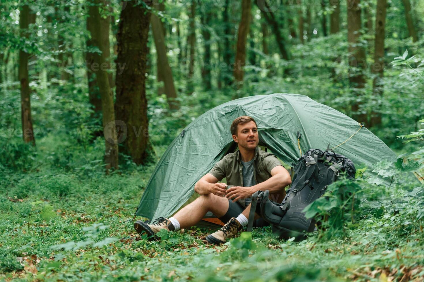 With ,cup, of, water. Sitting near the tent. Tourist in summer forest. Conception of exploration and leisure photo