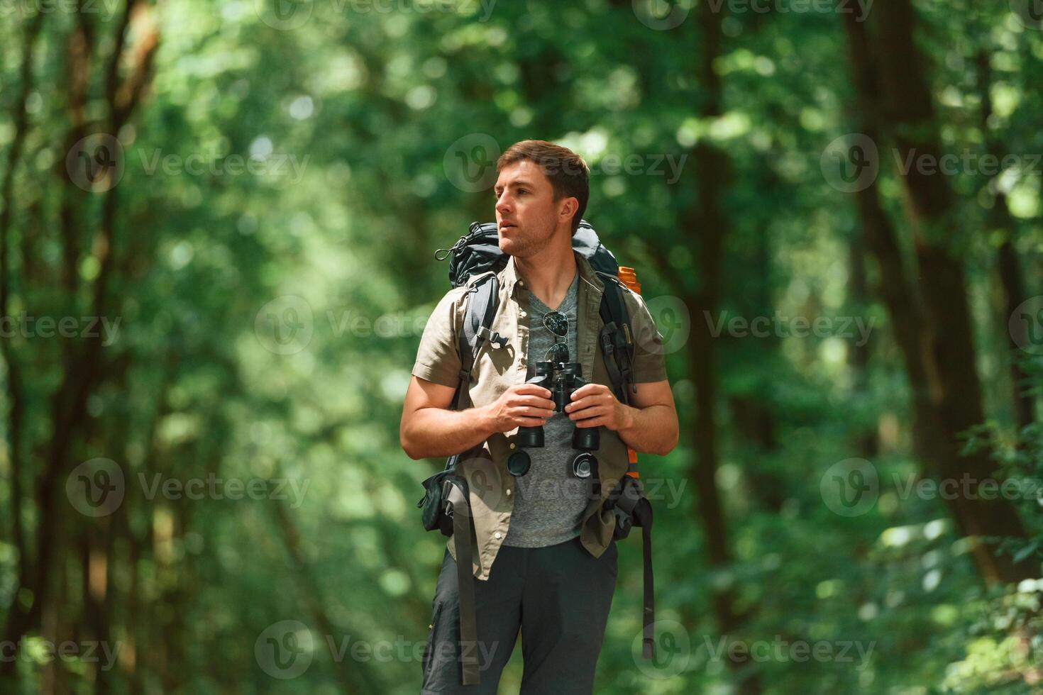 Standing ,and, holding binoculars. Tourist in summer forest. Conception of exploration and leisure photo