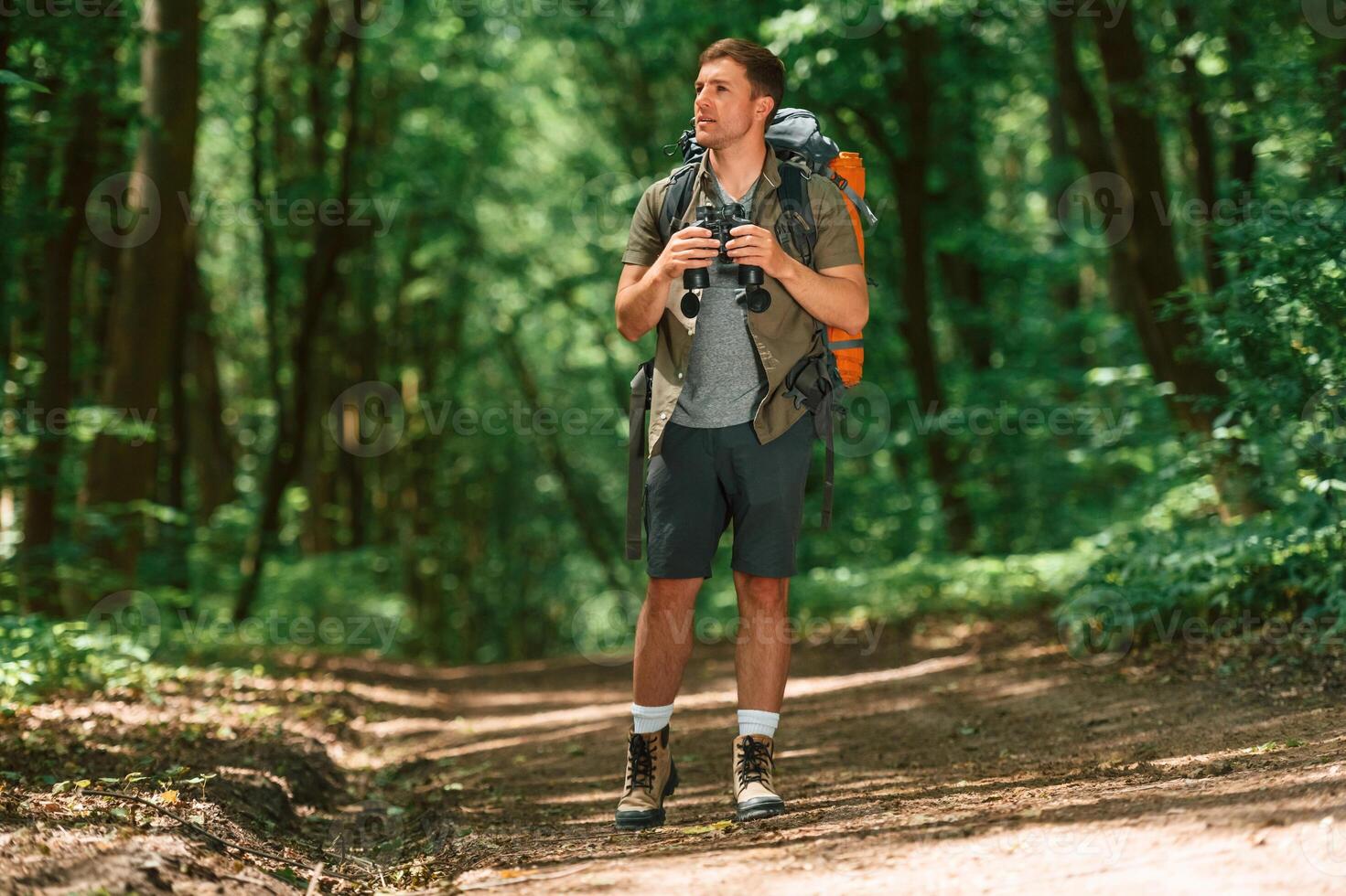Standing ,and holding ,binoculars. Tourist in summer forest. Conception of exploration and leisure photo