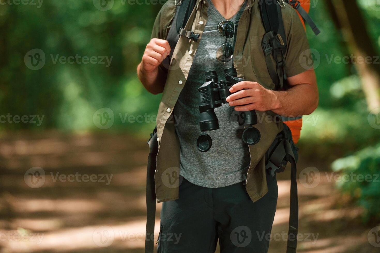 Holds, binoculars.. Close up view of tourist that is in summer forest photo