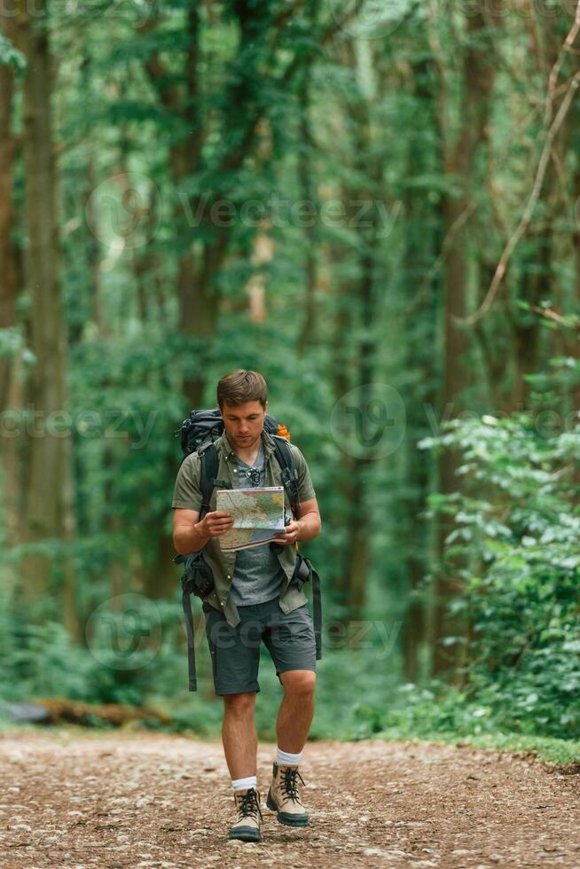 Walking forward with map in hands. Tourist in summer forest. Conception of exploration and leisure photo
