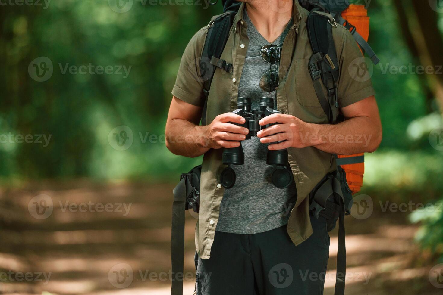 Holds binoculars.. Close up view of tourist that is in summer forest photo