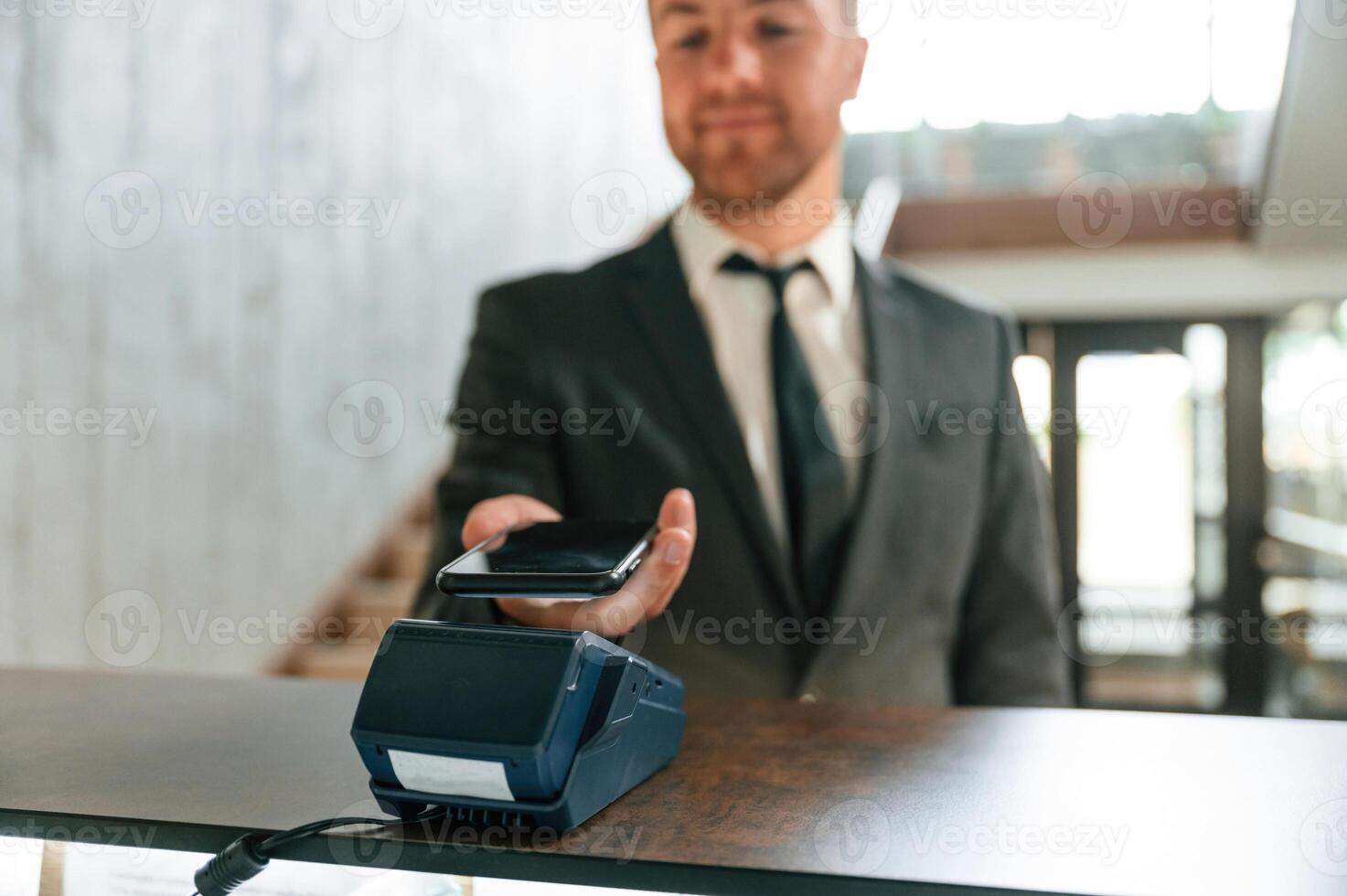 Making payment by using phone, and terminal. A man in a black jacket at the hotel reception photo