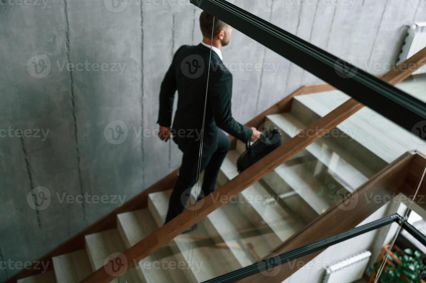 Walking ,up. Man, in business suit and tie with case in hands is on the stairs photo