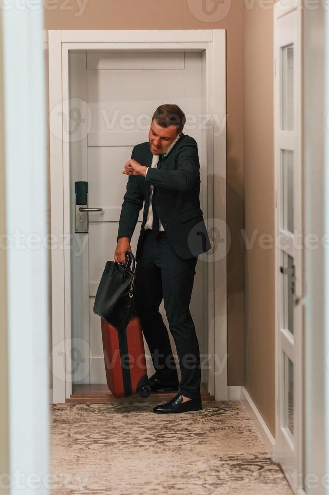 Entering the, appartment and and holds a suitcase in his hands. Handsome businessman is indoors in the hotel room photo