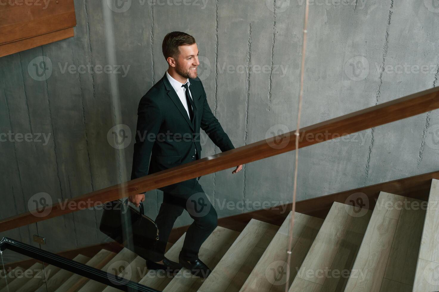 Walking up. Man ,in business suit and tie with case in hands is on the stairs photo