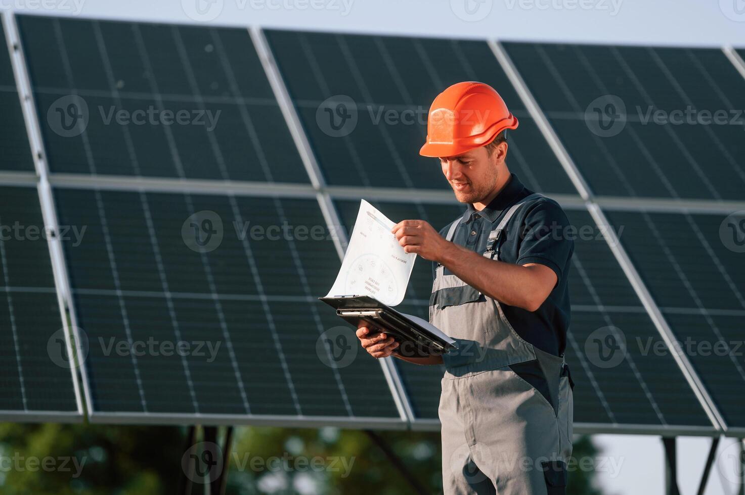 Notepad and digital tablet in hands. Man is doing operating and maintenance in solar power plant photo