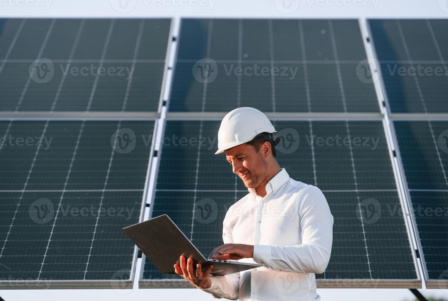Front view, holding laptop. Man, is doing operating and maintenance in solar power plant photo