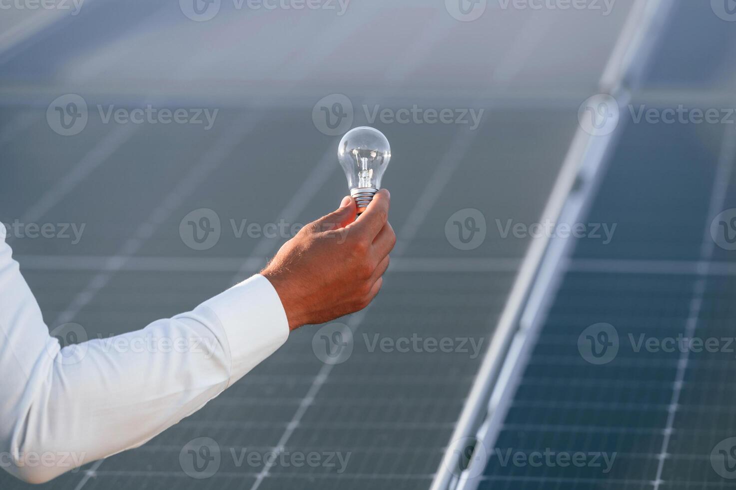 Close up view of man's hand ,that, is holding light bult in front of solar panel photo