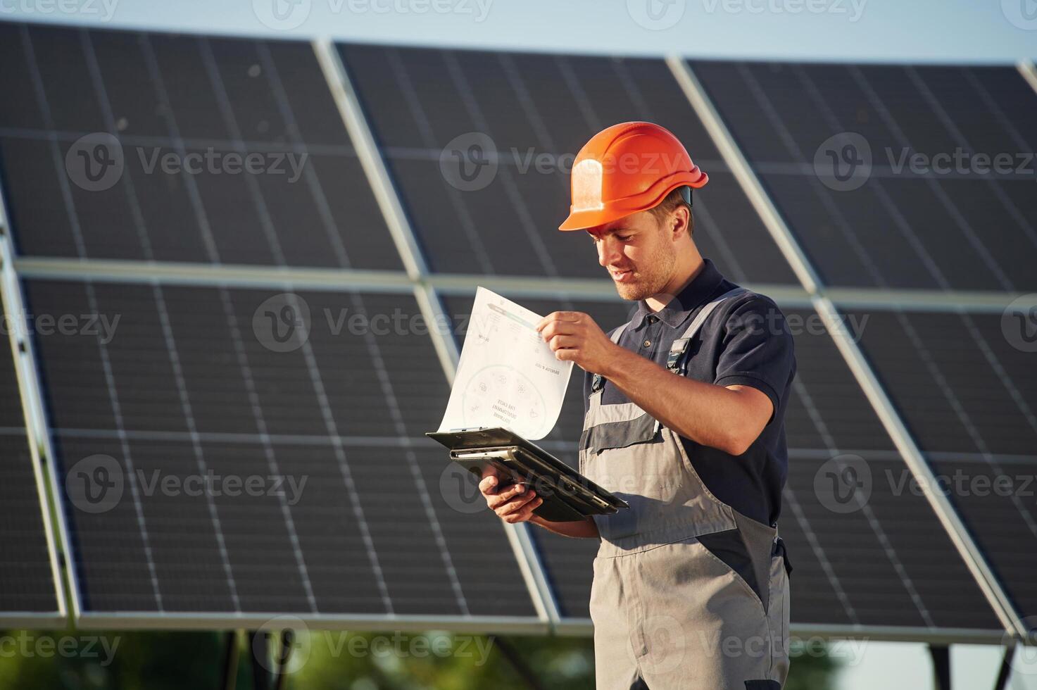 Notepad, and digital tablet in hands. Man is doing operating and maintenance in solar power plant photo