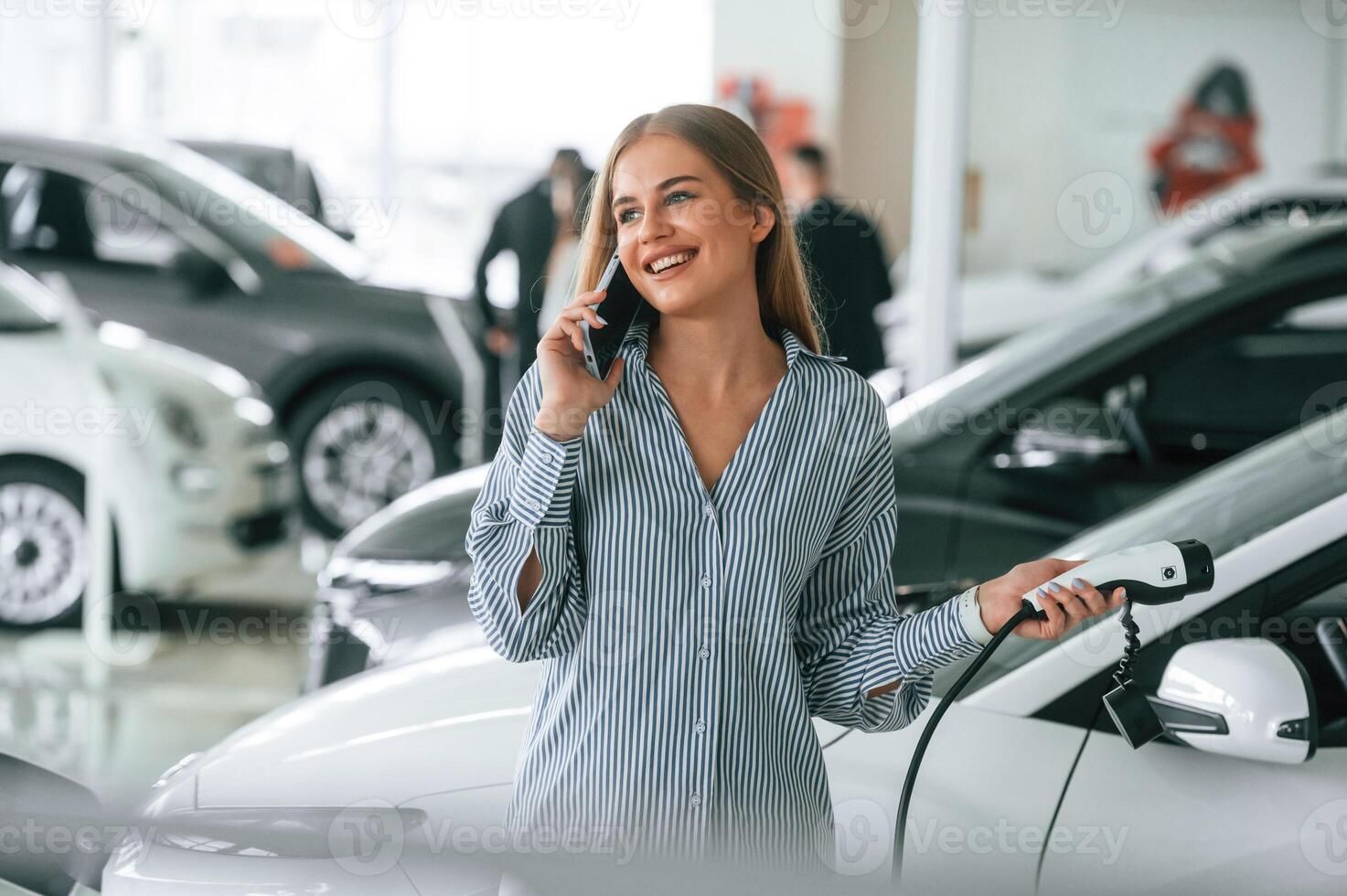 Talking by phone, and holding charger. Beautiful woman is indoors with the modern car photo