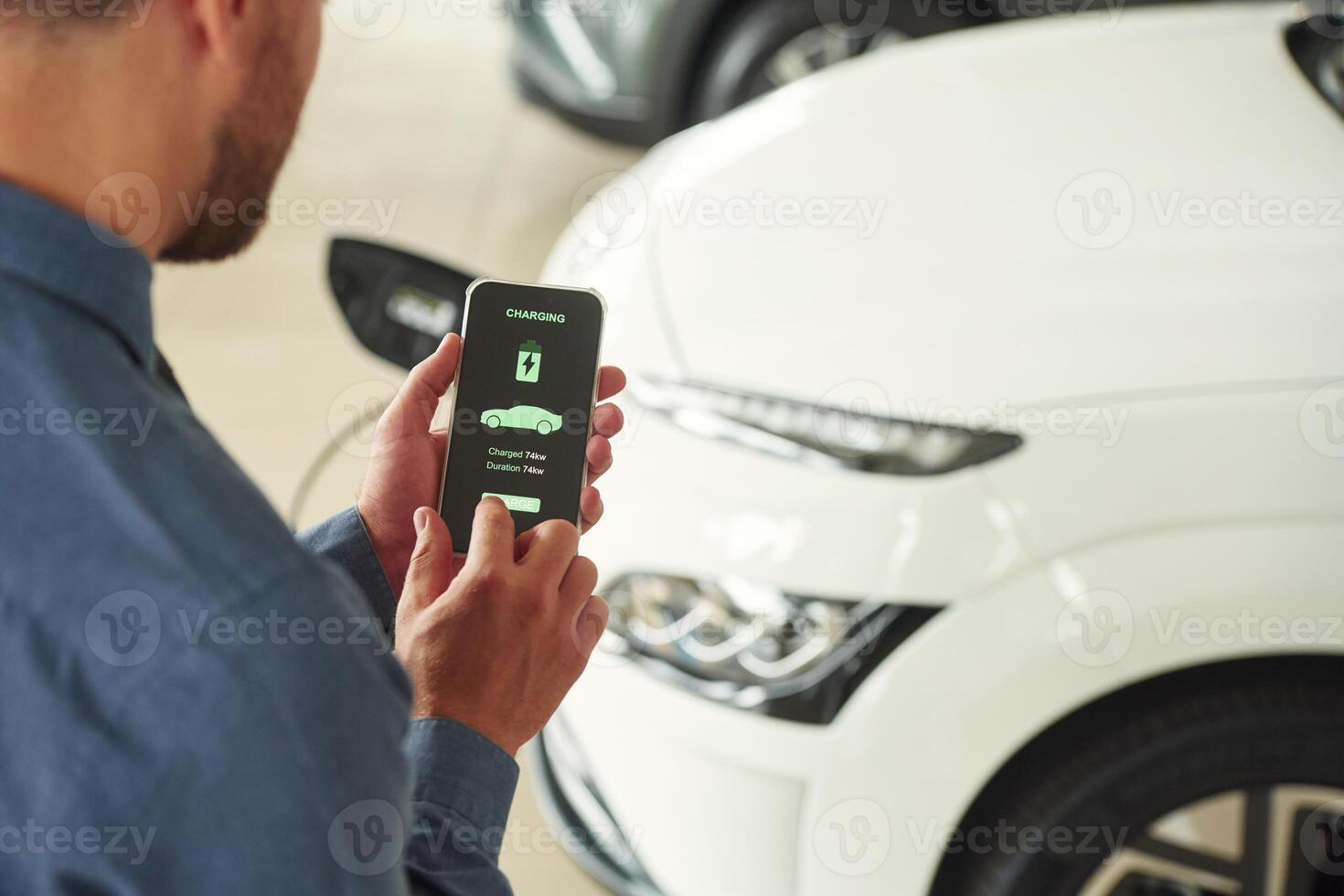 App interface of charging in smartphone. Handsome car dealership worker is with electric vehicle photo