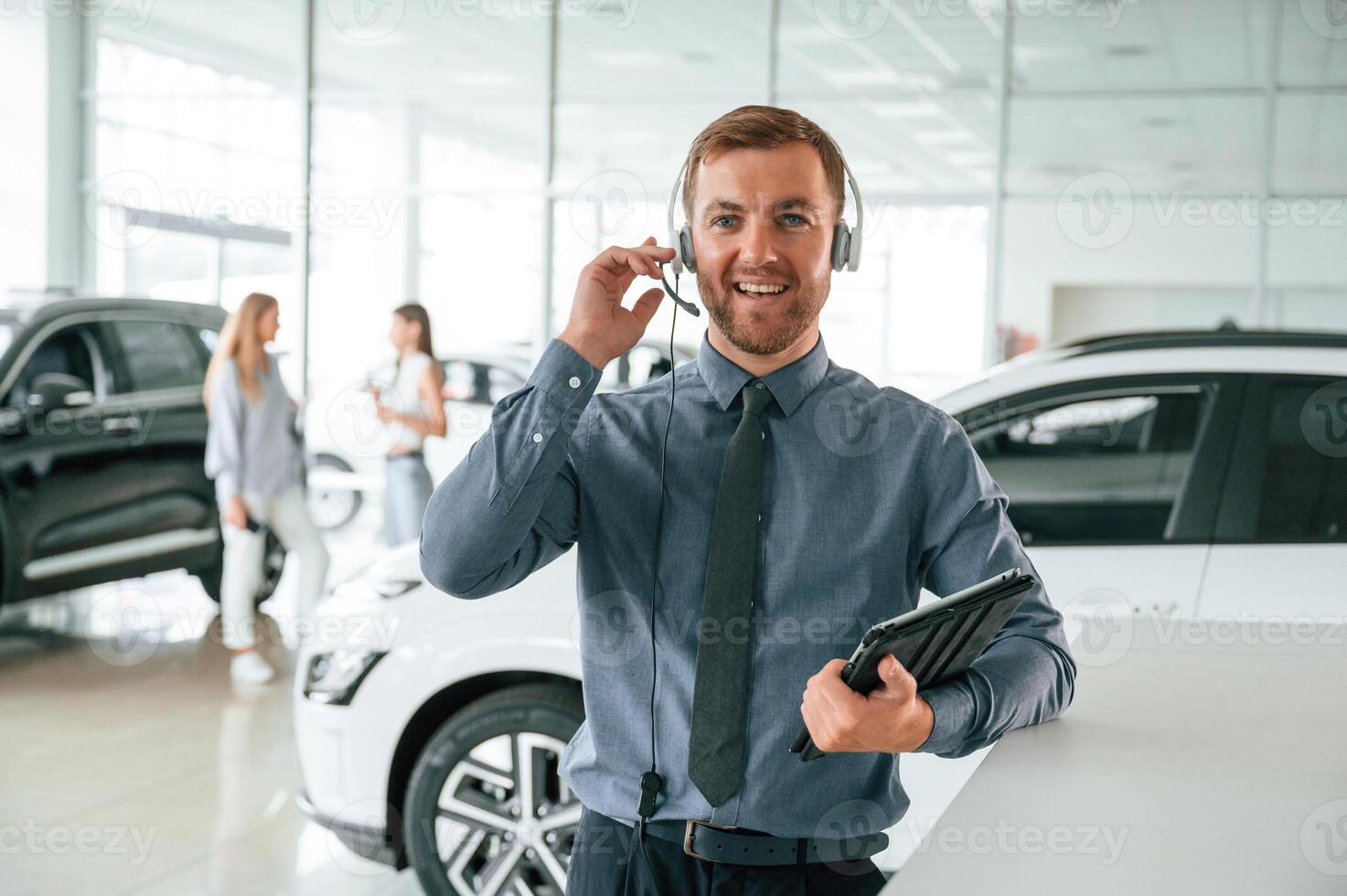 Manager, is in the headphones, and with notepad. Handsome car dealership worker is with electric vehicle photo