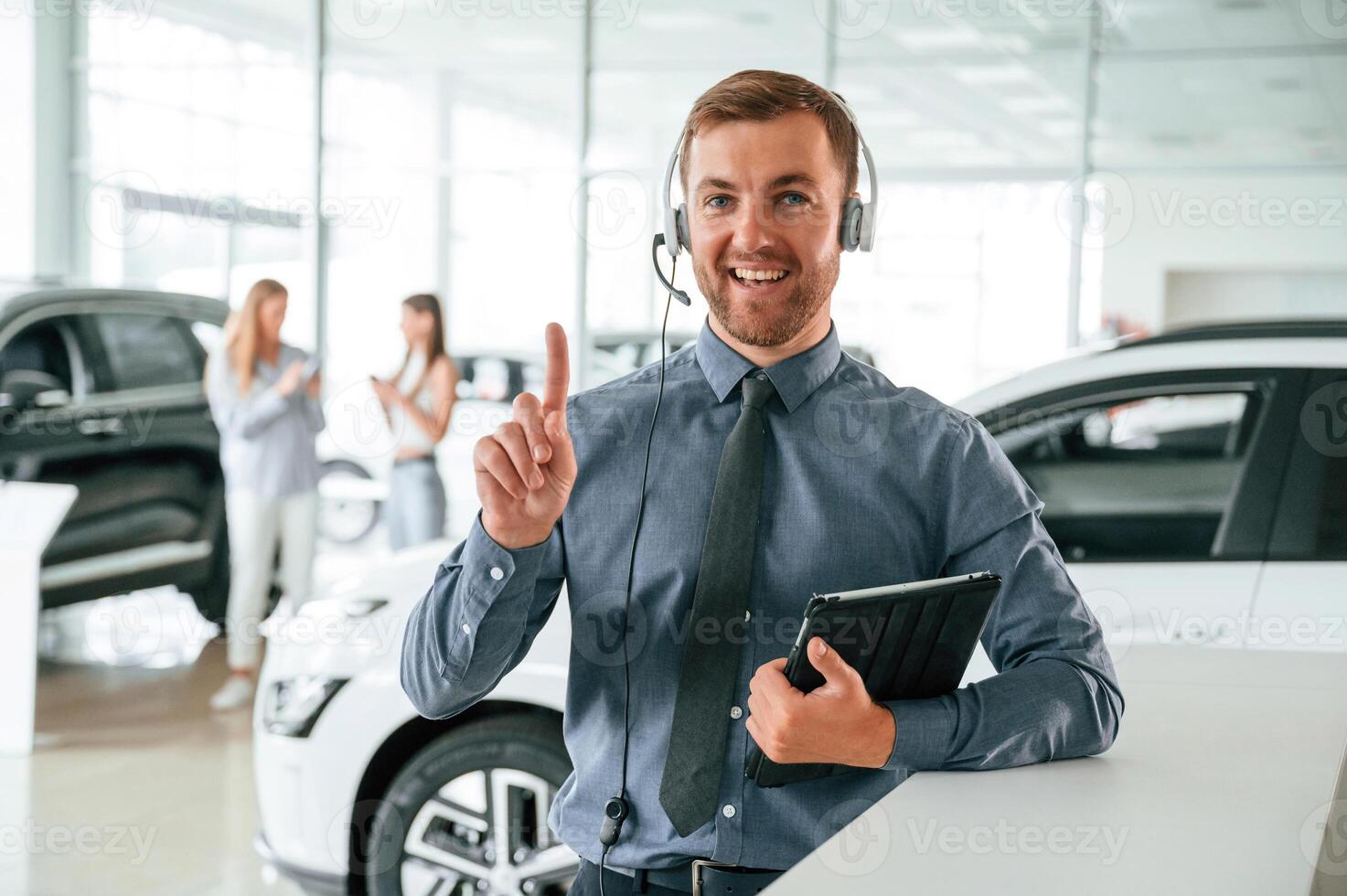 Manager, is in the headphones and with notepad. Handsome car dealership worker is with electric vehicle photo