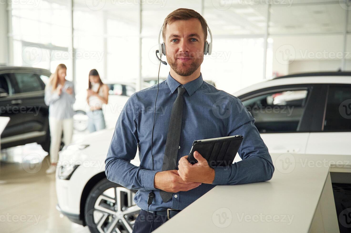 Manager is ,in the headphones and with notepad. Handsome car dealership worker is with electric vehicle photo