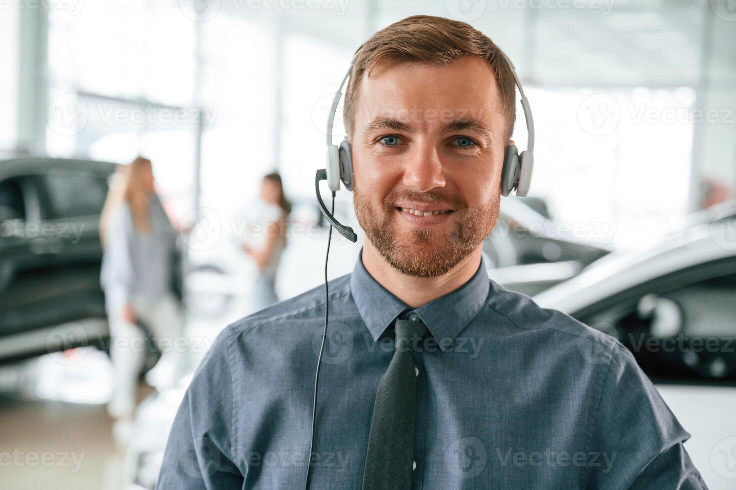 Portrait ,of handsome car dealership worker that is with electric vehicle. In headphones photo