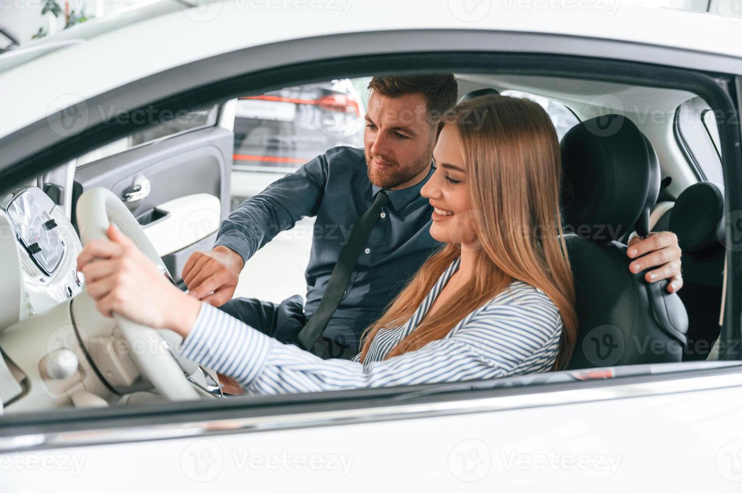 Explainin,g how ,automobile works. Man in formal clothes is with woman customer with the electric car photo