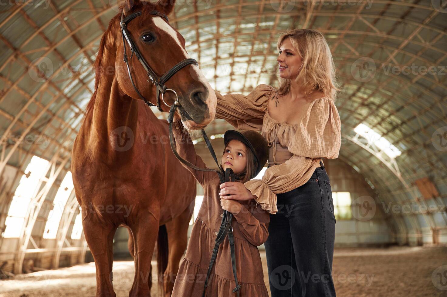 Woman with her little daughter is with horse indoors photo