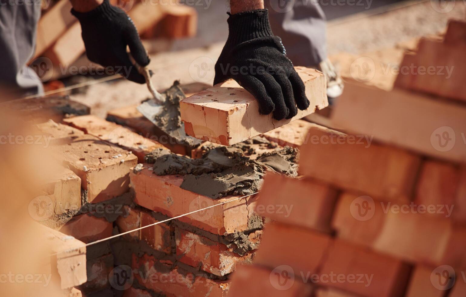 In, gloves, holding brick. Close up view of man that is working on the construction site photo