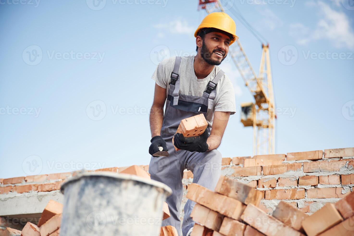 Blue, sky, and crane is behind. Handsome Indian man is on the construction site photo