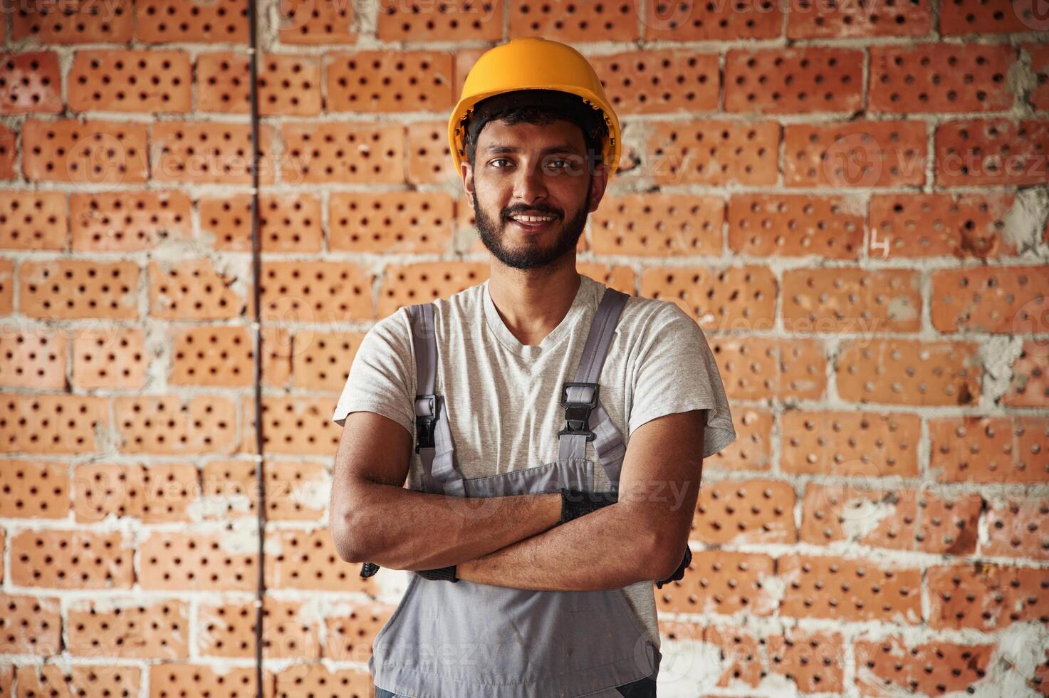 Indoors against brick wall,. Handsome Indian man is on the construction site photo